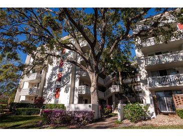 Low angle shows condo building with white balconies, beautiful mature tree, and colorful flowers at 2630 Pearce Dr # 104, Clearwater, FL 33764