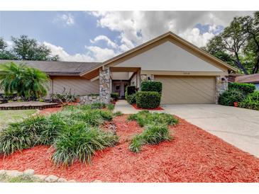 Charming home featuring a stone accent facade, a well-manicured lawn, and landscaping with vibrant red mulch at 3310 Tanglewood Trl, Palm Harbor, FL 34685