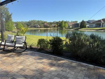 Enjoy the beautiful lake view from this gorgeous brick patio with rocking chairs and lush landscaping at 4810 Diamonds Palm Loop, Wesley Chapel, FL 33543