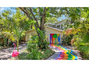 Unique home exterior showcasing a colorful painted driveway and garage doors, surrounded by lush greenery and palm trees at 6014 Luana S Ln, Gulfport, FL 33707