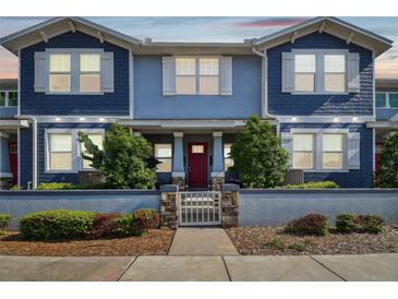 Charming blue townhome featuring a red door, white trim, and a landscaped front yard with a decorative fence at 414 Finn Way # 4, Dunedin, FL 34698