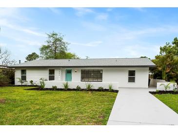 Charming single-story home featuring a manicured lawn and a bright, welcoming turquoise front door at 1886 San Mateo Dr, Dunedin, FL 34698