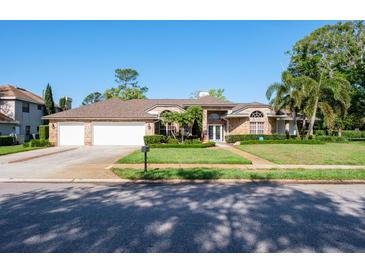 Charming brick home with a lush green lawn, manicured landscaping, and a three car garage at 2990 Eagle Estates W Cir, Clearwater, FL 33761