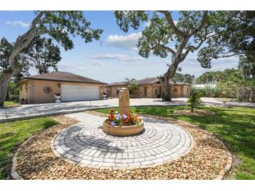 Beautiful single-story home with a circular flower fountain in the front yard and mature shade trees on a sunny day at 6732 Udell Ln, Hudson, FL 34667