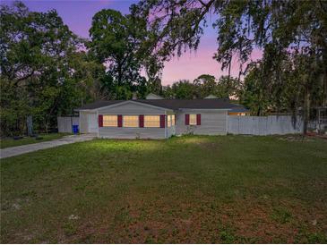 Charming single story home with mature trees, light siding, red shutters, green lawn and long driveway at 34477 Poinsettia Pl, Dade City, FL 33523
