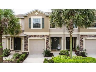 Charming townhome exterior with stone accents, a two-car garage, and tropical landscaping at 10425 Yellow Spice Ct, Riverview, FL 33578
