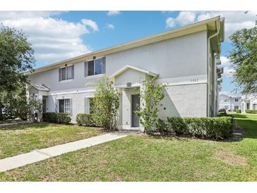 Light grey townhome featuring a well-manicured lawn and flower bushes next to the front door at 7303 E Bank Dr, Tampa, FL 33617