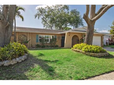 Charming home boasts a well-manicured lawn, mature trees, and an inviting, arched entryway at 8350 Monarch Cir, Seminole, FL 33772