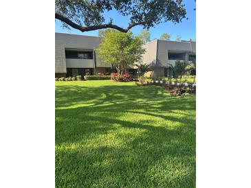 Exterior view of a well-maintained two-story building with lush green lawn and beautiful landscaping at 36750 Us 19 N # 5-111, Palm Harbor, FL 34684