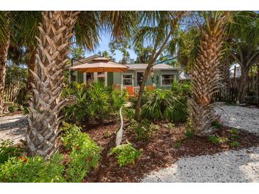 Charming home with tropical landscaping, featuring palm trees and a cozy seating area with an umbrella at 8403 W Gulf Blvd, Treasure Island, FL 33706