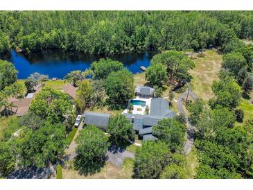 Expansive aerial view of a home with a pool, nestled among lush greenery and bordering a tranquil lake at 898 Cypress Lakeview Ct, Tarpon Springs, FL 34688