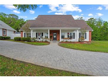 Charming single-story home featuring a brick and white exterior, covered porch with swings, and a brick-paved driveway at 12345 Citrus Way, Brooksville, FL 34601
