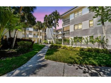 Multi-story condo with a sidewalk and tropical landscaping, including palm trees, bushes, and well-maintained grass at 2650 Countryside Blvd # C203, Clearwater, FL 33761