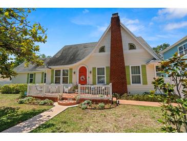 Charming home featuring a brick chimney, an inviting front porch, and vibrant green shutters against a light-yellow facade at 1603 S Arrawana Ave, Tampa, FL 33629