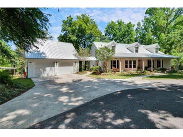 Inviting white home with metal roof, lush landscaping, and a spacious driveway leading to an attached garage at 16420 Iola Woods Trl, Dade City, FL 33523