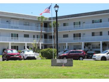 Three-story condo building with an American flag in front, cars parked in the front and a manicured lawn at 2001 World Parkway Blvd # 49, Clearwater, FL 33763