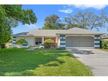Charming single-story home featuring a manicured lawn, colorful accents, and an attached two-car garage at 8195 Wooden Dr, Spring Hill, FL 34606