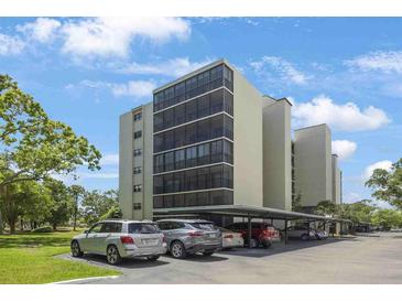 Low-angle view of a multi-story condo building with covered parking beneath it in front of lush, green trees at 2900 Cove Cay Dr # 1B, Clearwater, FL 33760