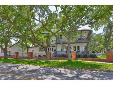 Charming two-story home with a front porch, a balcony, a brick fence, and mature trees at 2802 Old Bayshore Way, Tampa, FL 33611
