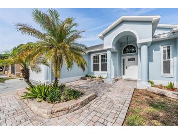 Inviting home entrance with a brick walkway, front yard landscaping, and an arched doorway framed by pillars at 7039 Woodibis Dr, New Port Richey, FL 34654