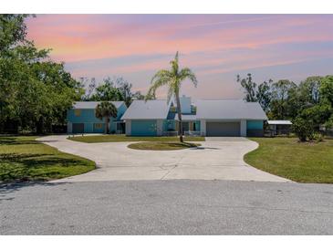 Charming light-blue home with a circular driveway, mature palm tree, and ample parking at 1305 Greenfield Cir, Venice, FL 34292