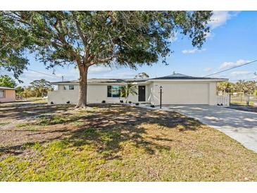 A charming single-story home features a large front yard with a well-manicured lawn and mature trees at 1499 Janet Pl, Englewood, FL 34223