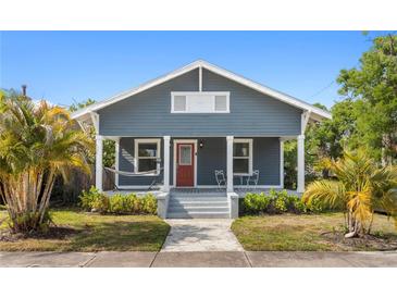 Charming blue home featuring a cozy front porch, red door, and lush landscaping under a clear blue sky at 107 W Amelia Ave, Tampa, FL 33602