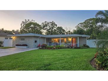 Charming single-story home with stone facade, manicured lawn, and colorful flower beds, complemented by a vibrant red front door at 7301 2Nd S Ave, St Petersburg, FL 33707