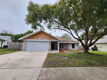Charming single-story home with a gray exterior, stone accents, and a large tree in the front yard at 12312 Golden Oak Cir, Hudson, FL 34669