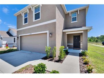 Two story home features a two car garage, neutral stucco facade, manicured lawn, and covered front porch at 16894 Delia St, Wimauma, FL 33598