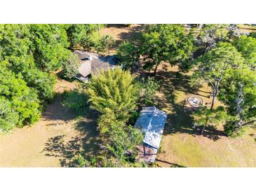 Aerial view highlighting the home nestled among mature trees, outdoor fire pit, shed, and serene surroundings at 27477 Old Trilby Rd, Brooksville, FL 34602