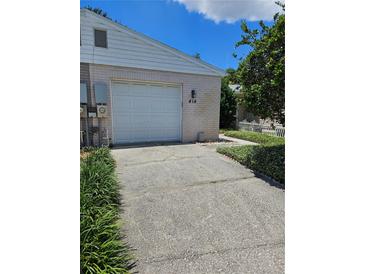 Home exterior with white garage door, number 414, and cracked driveway lined with manicured greenery at 414 Danube Ave, Tampa, FL 33606