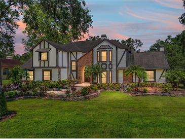 Charming Tudor-style home featuring a brick entrance, lush landscaping, and well-manicured lawn at dusk at 13004 Bell Creek Chase, Riverview, FL 33569