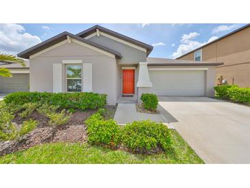 Charming single-story home featuring a well-manicured lawn, tasteful landscaping and an inviting orange front door at 16665 Delia St, Wimauma, FL 33598