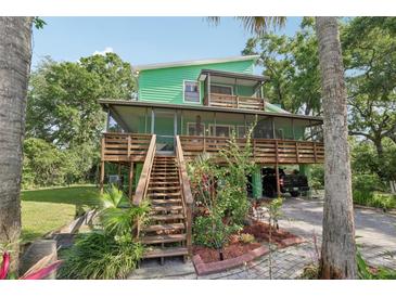 Two-story green house with multiple decks, surrounded by lush greenery and mature trees at 8614 Hibiscus Dr, Tampa, FL 33637