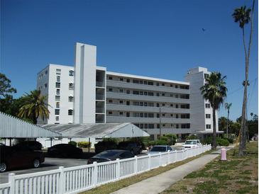 Condo complex with white exterior, covered parking, white picket fence, palms, and blue skies at 200 N Betty Ln # 5F, Clearwater, FL 33755