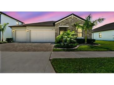 Beautiful single-story home featuring stone accents, a two-car garage, manicured landscaping, and a brick paved driveway at 21506 Snowy Orchid Ter, Land O Lakes, FL 34637