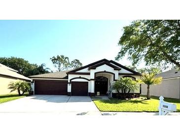 Charming single-story home featuring a two-car garage, manicured lawn, and tropical landscaping at 5554 Riva Ridge Dr, Wesley Chapel, FL 33544