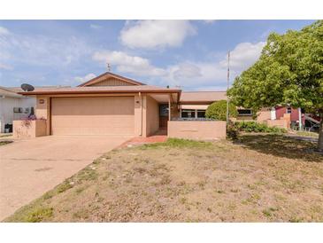 Tan single Gathering home showcasing an attached garage, covered entry, and a well-maintained yard at 9205 Ledgestone Ln, Port Richey, FL 34668