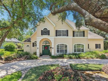 Stately two-story home featuring a lush front yard, mature trees, and an arched entrance with a green front door at 1927 Curry Rd, Lutz, FL 33549