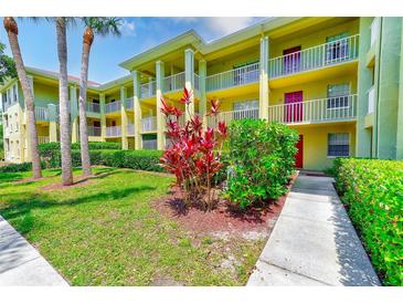 Condo building featuring a yellow exterior, lush landscaping, and white railings at 2690 Coral Landings Blvd # 122, Palm Harbor, FL 34684