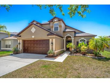 Inviting exterior with a two-car garage, arched entryway, fresh landscaping, and a well-manicured lawn at 8103 Tar Hollow Dr, Gibsonton, FL 33534