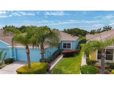 Charming blue home featuring a two-car garage, lush landscaping, and picturesque palm trees in a well-maintained community at 11457 Captiva Kay Dr, Riverview, FL 33569