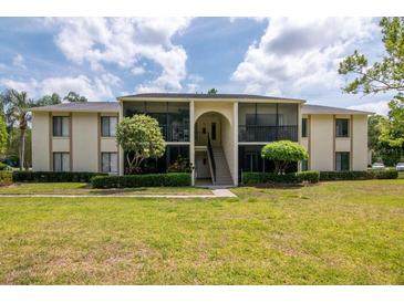 Low-angle view of the neutral-toned exterior of this two-story condominium building with lush landscaping and a central staircase at 1400 Pine Glen Ln # B2, Tarpon Springs, FL 34688