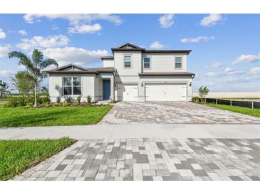 Two-story home featuring a 3 car garage, brick paver driveway, and a blue front door at 13631 Sunlight Meadow Dr, Riverview, FL 33578