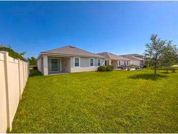 View of the grassy backyard and exterior of the home with white fence at 10729 Planer Picket Dr, Riverview, FL 33569