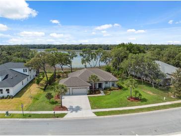 Beautiful single-story home with a well-manicured lawn, mature trees, and a scenic lake view in the background at 15615 Serengeti Blvd, Spring Hill, FL 34610