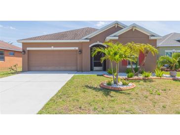 Charming home features a well-manicured lawn, mature palm trees, and a two-car garage, offering a welcoming curb appeal at 711 Parker Den Dr, Ruskin, FL 33570