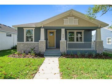 Charming home featuring a covered porch, stone accents, fresh landscaping, and a welcoming yellow front door at 936 57Th N Ave, St Petersburg, FL 33703