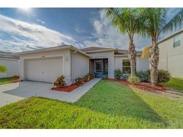 Charming single-story home featuring a well-manicured lawn, lush landscaping, and lovely palm trees at 15430 Long Cypress Dr, Ruskin, FL 33573